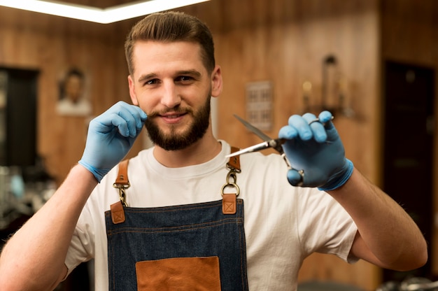 Free photo front view of male barber holding scissors in the barbershop