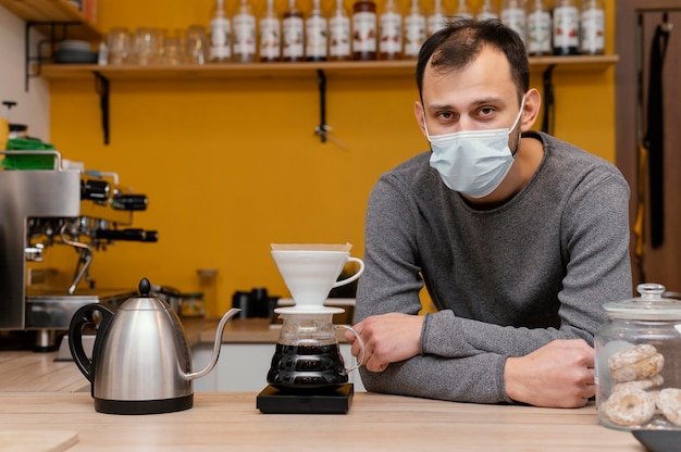 Free photo front view of male barista with medical mask posing in the coffee shop