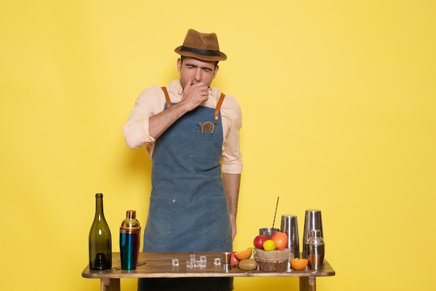 Free photo front view male bartender in front of table with drinks and shakers yawning on yellow wall drink night alcohol bar color club male