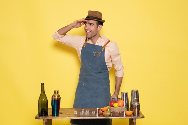 Front view male bartender in front of table with drinks and shakers on yellow wall drinks night alcohol bar color club male