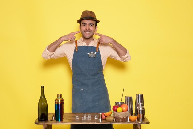 Front view male bartender in front of table with drinks and shakers on yellow wall night alcohol bar male drink club