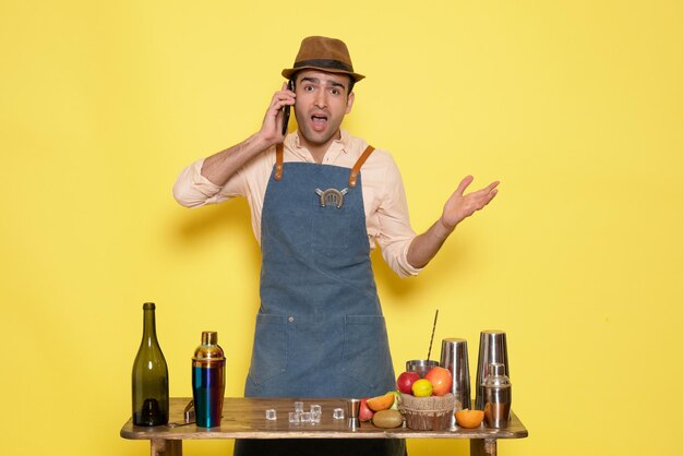 Front view male bartender in front of table with drinks and shakers on yellow wall night alcohol bar male drinks club