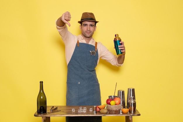 Front view male bartender in front of table with drinks and shakers on a yellow wall night alcohol male club bar drink