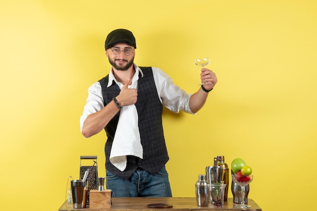 Front view male bartender in front of table with shakers cleaning glasses on a yellow wall bar alcohol night youth drink club