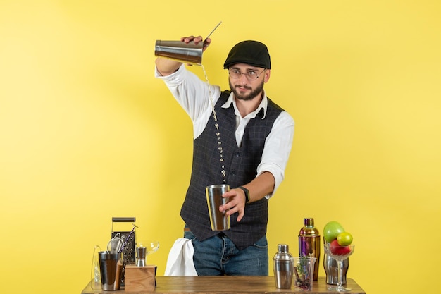 Free photo front view male bartender in front of table with shakers making a drink on the yellow wall bar alcohol night youth drink club