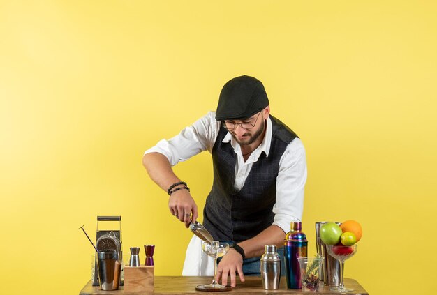 Front view male bartender in front of table with shakers preparing drink on yellow wall bar alcohol drink night club youth