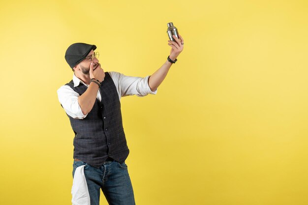 Front view male bartender holding little silver shaker on yellow wall model drink work club male night job