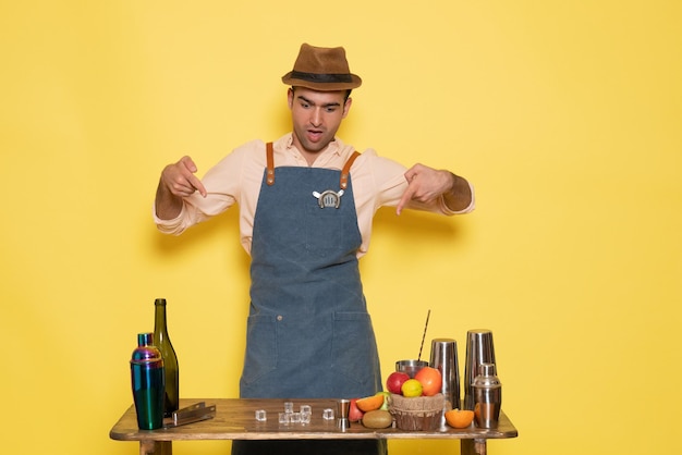 Free photo front view male bartender standing in front of desk with drinks and ice on yellow wall night club bar male drink