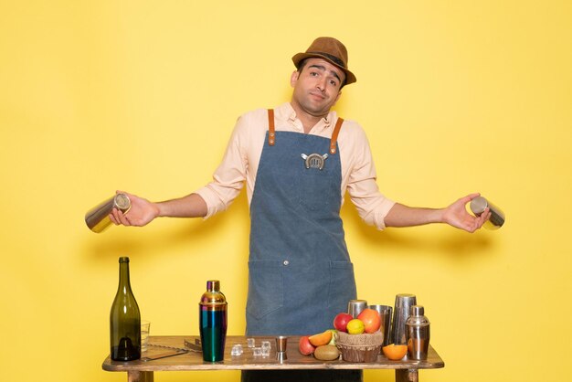 Front view male bartender working with shaker and making drink on yellow floor night alcohol bar club male drink