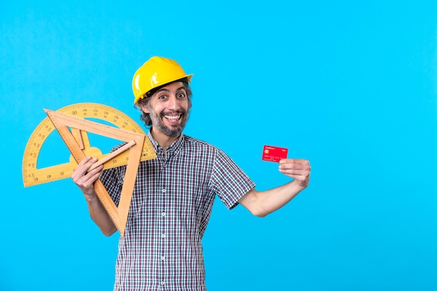 Front view male builder holding wooden figures and bank card on blue