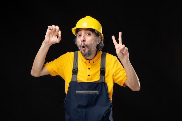 Front view male builder in uniform on black wall