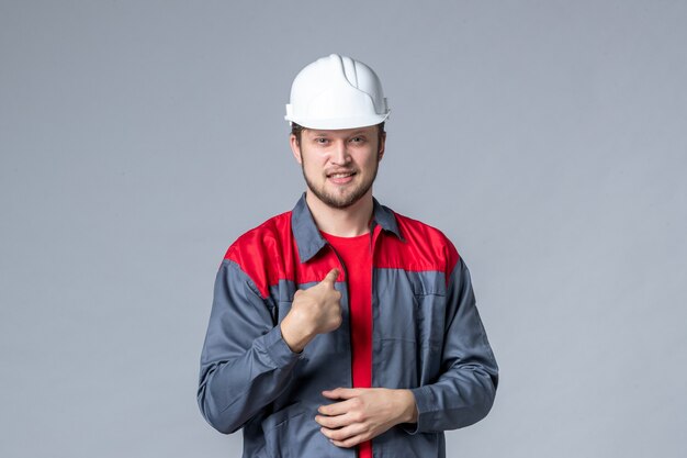 front view male builder in uniform and helmet on gray background