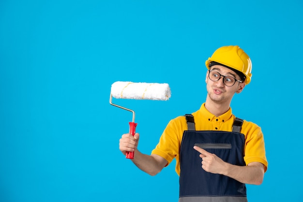 Free photo front view male builder in uniform and helmet with paint roller on blue