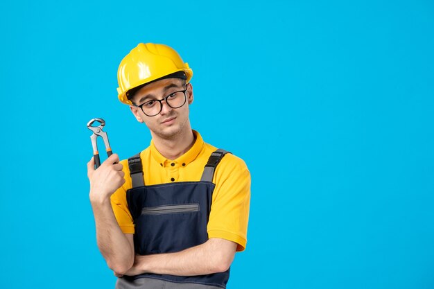 Front view of male builder in uniform and helmet with pliers on blue wall