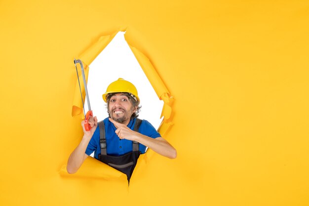 Free Photo front view male builder in uniform holding bowsaw on the yellow background