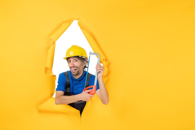 Front view male builder in uniform holding bowsaw on the yellow background