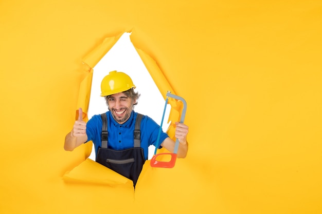 Front view male builder in uniform holding bowsaw on yellow background