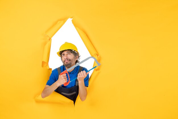 Front view male builder in uniform holding bowsaw on yellow background