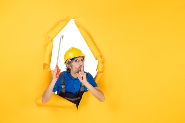 Front view male builder in uniform holding bowsaw on yellow background