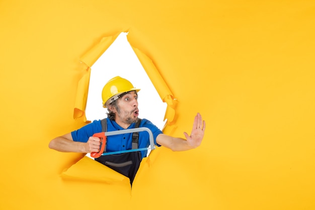 Free photo front view male builder in uniform holding bowsaw on yellow background