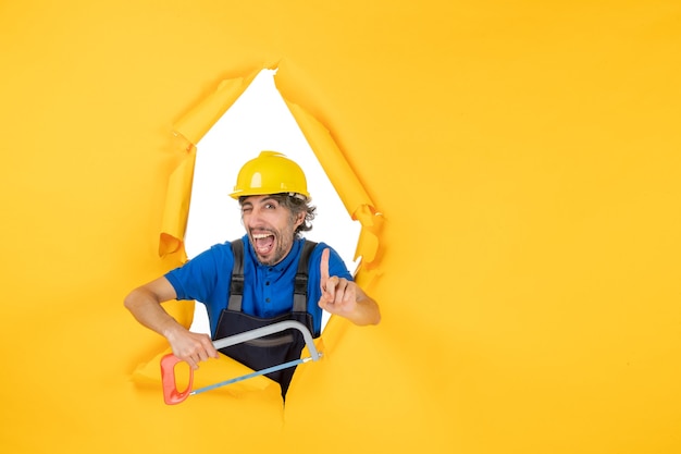 Front view male builder in uniform holding bowsaw on yellow background