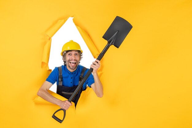 Front view male builder in uniform holding shovel on yellow background