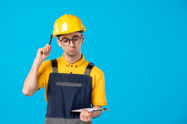 Front view of male builder in uniform with file note in his hands on blue wall