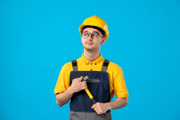 Front view of male builder in uniform with hammer in his hands on blue wall