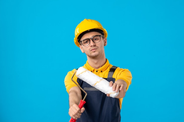 Front view of male builder in uniform with paint roller on blue wall