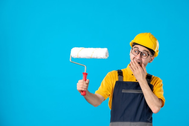 Free photo front view of male builder in uniform with paint roller in his hands on blue wall