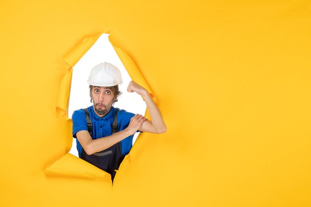 Front view male builder in uniform on the yellow background