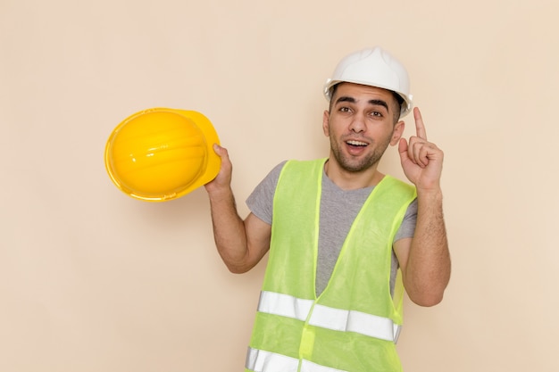 Free photo front view male builder in white helmet holding yellow helmet on the cream background