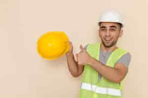 Free photo front view male builder in white helmet holding yellow helmet on light background