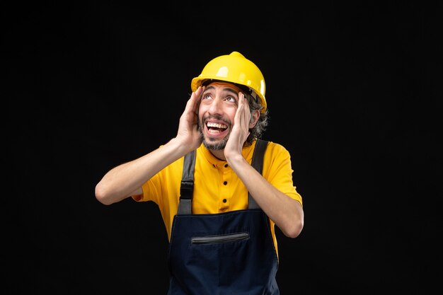 Front view of male builder in yellow uniform on black wall