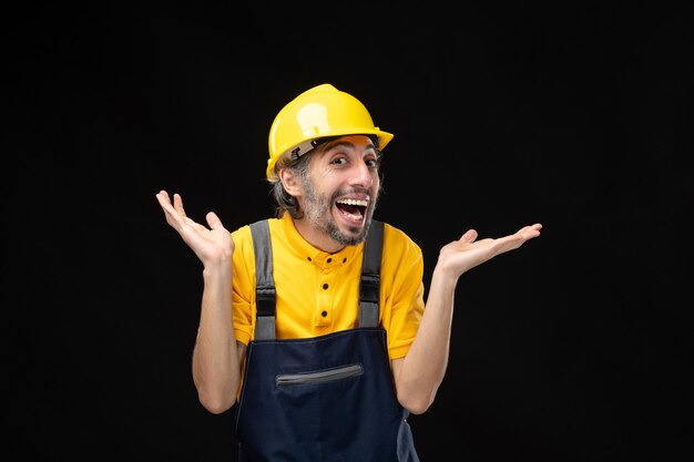 Front view of male builder in yellow uniform on black wall