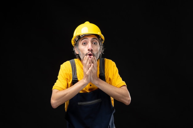 Front view of male builder in yellow uniform on black wall