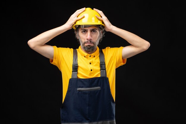 Front view of male builder in yellow uniform on black wall