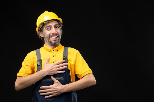 Front view of male builder in yellow uniform on black wall