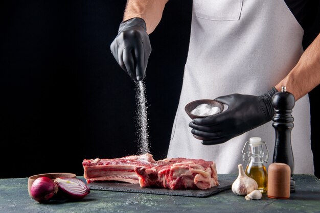 Front view male butcher salting meat on dark surface