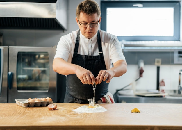 Front view of male chef breaking egg over flour to create dough