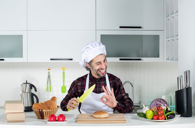 Front view of male chef holding yellow knife making okey sign in the kitchen