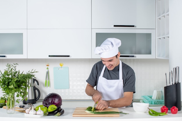 Front view male chef in uniform chopping greens behind kitchen table