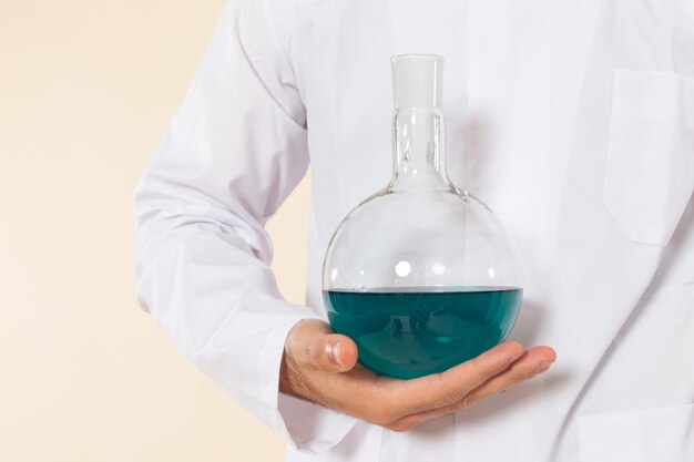 Front view male chemist in white special suit holding flask with blue solution on the cream desk science lab experiment chemistry