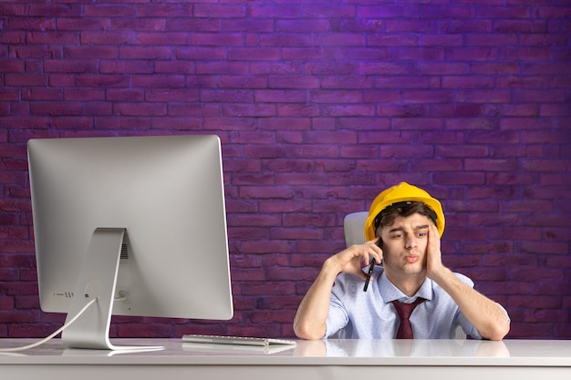 Front view male constructor behind office desk talking at phone