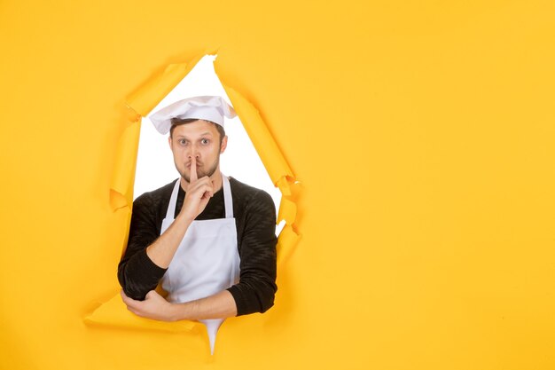 Front view male cook in white cape and cap on yellow ripped cuisine color job kitchen food man