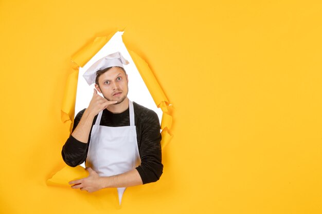 Front view male cook in white cape and cap on yellow ripped job color white photo kitchen man cuisine