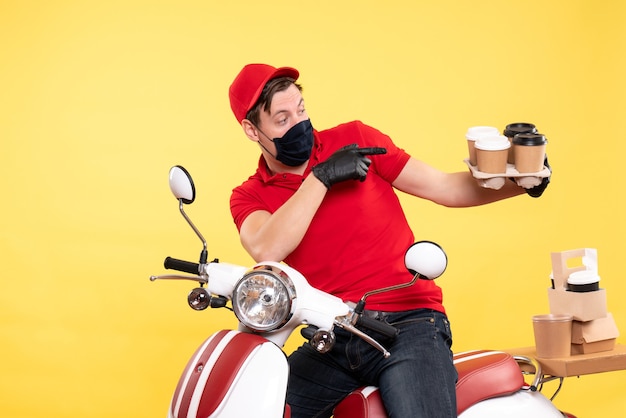 Front view male courier on bike in mask with coffee on yellow 