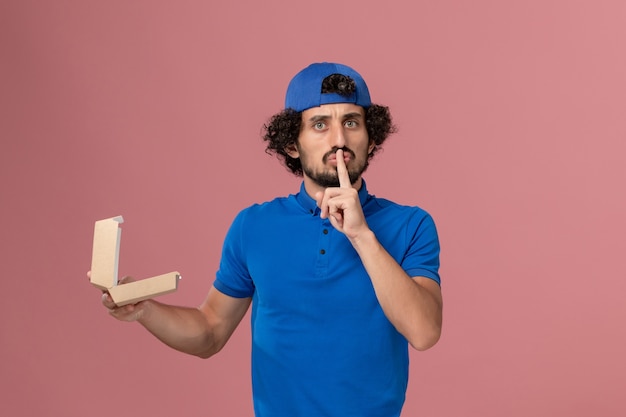 Free Photo front view male courier in blue uniform and cape holding little delivery food package on the pink wall