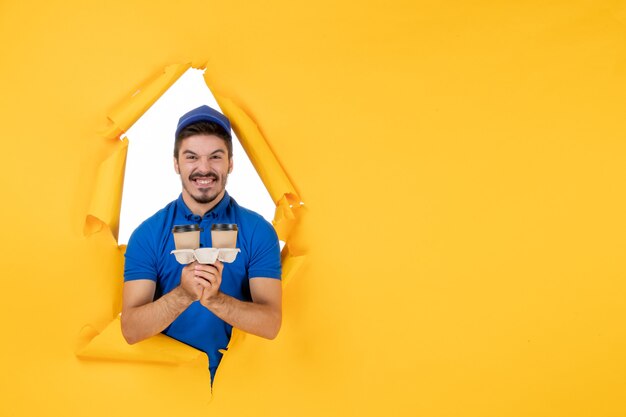 Free Photo front view male courier in blue uniform holding coffee cups on the yellow space