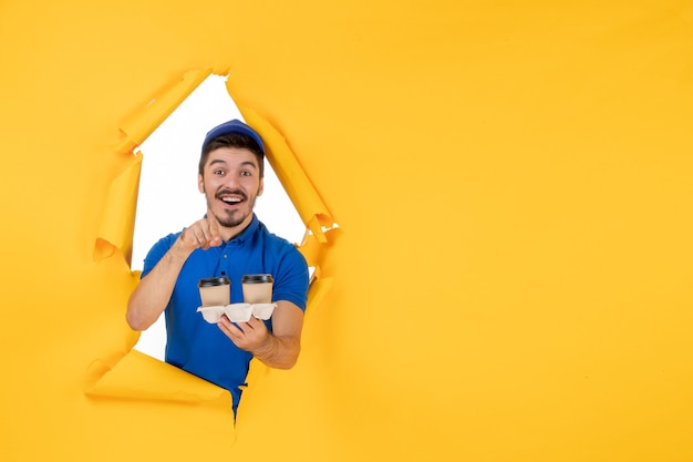 Free Photo front view male courier in blue uniform holding coffee cups on the yellow space